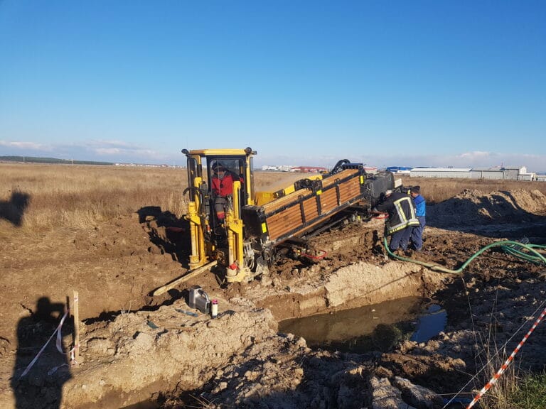 Utilaj HDD realizând foraj orizontal dirijat fără săpătură sub drum